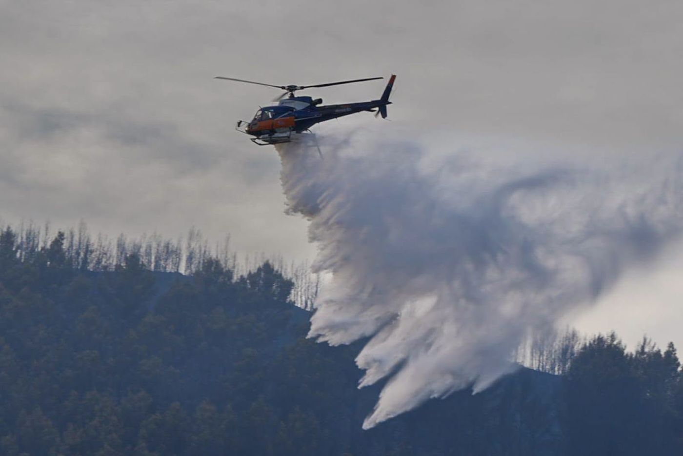 Een blushelikopter van de Sécurité civile boven een beboste heuvelrug in de Var tijdens een natuurbrand. Foto Sapeurs-Pompiers du Var (SDIS 83).